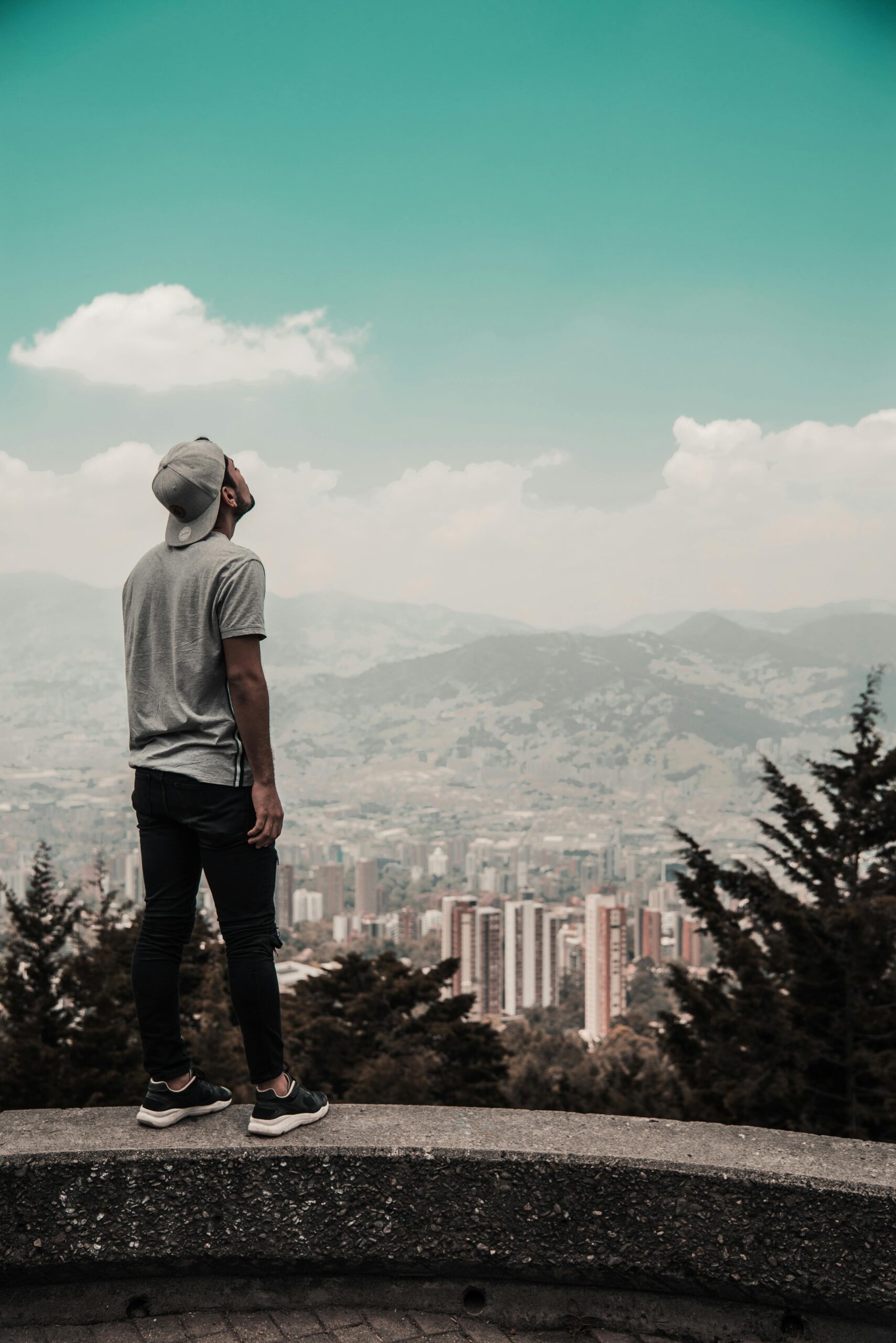Man in casual attire gazes over Medellín's skyline, capturing the city's urban charm and natural backdrop.