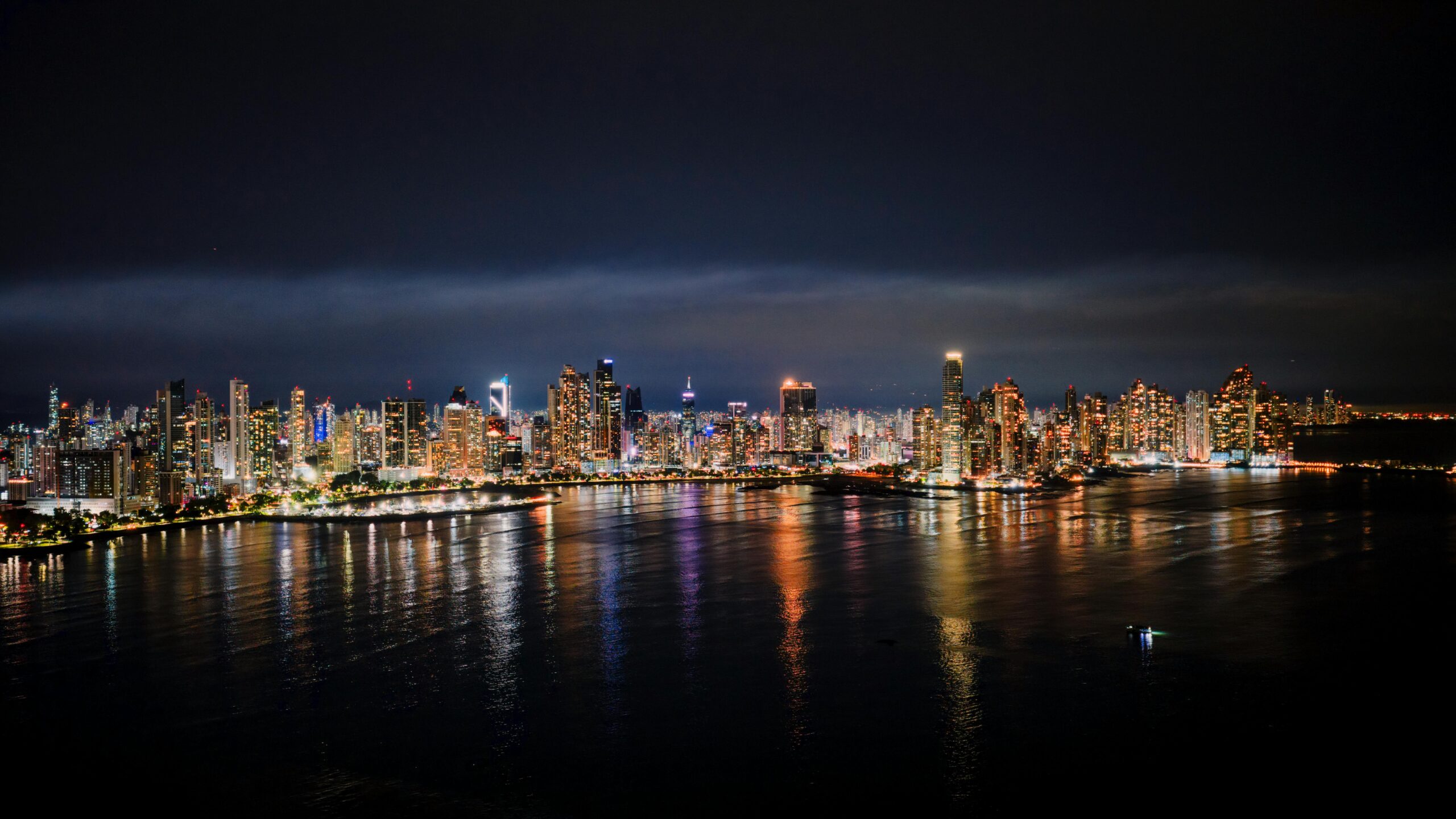 Nighttime aerial view of Panama City's illuminated skyline reflecting on the water.