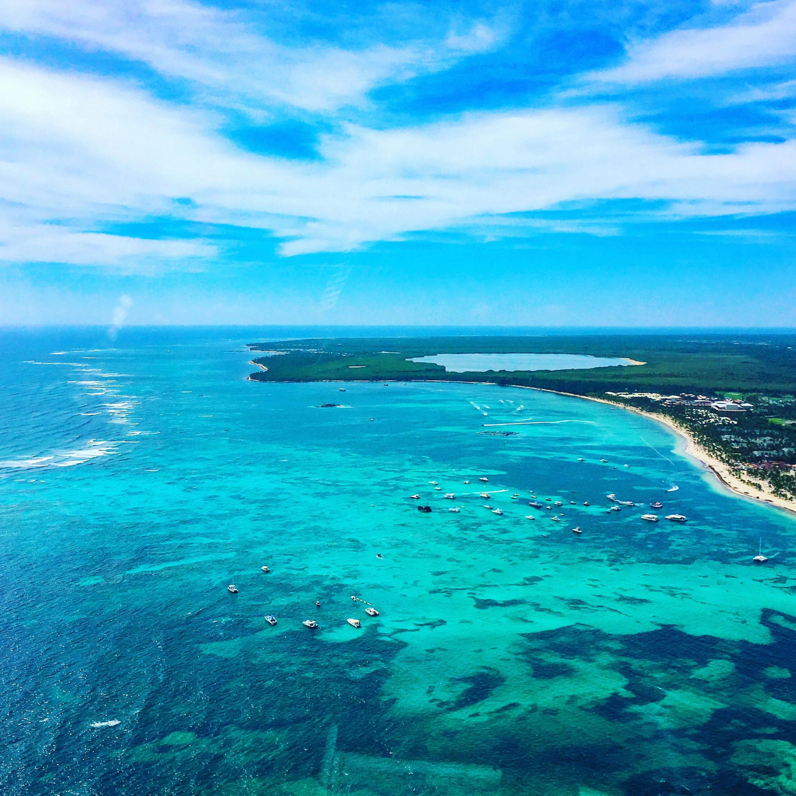 Drone view of peaceful blue sea with sailing small boats near coastal settlement on tropical lush island on sunny day